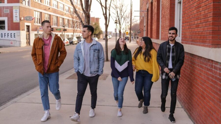 Group of five students walking together on a city sidewalk near campus buildings