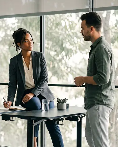 A woman and a man engaged in discussion at a meeting table in a professional setting.