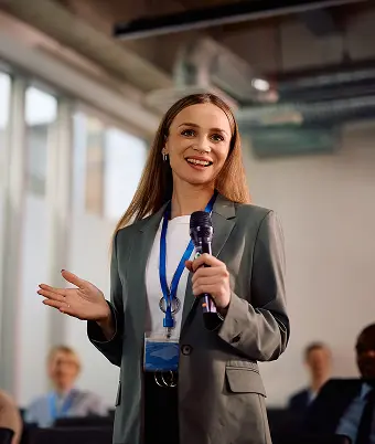 A professional woman in a business suit stands at a podium, addressing an audience during a formal speech.