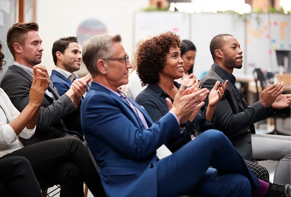A gathering of individuals in a meeting, actively applauding to express approval and enthusiasm for the discussion.