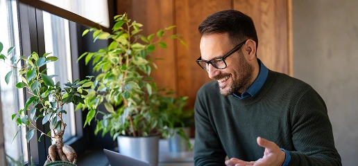 A man wearing glasses and a sweater sits at a desk, focused on his laptop.