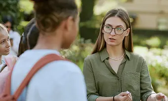 A woman wearing glasses engages in conversation with a group of attentive individuals.
