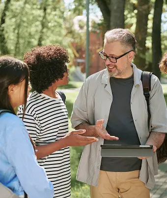 A man engages with a group of students in a park, sharing knowledge and fostering discussion in an outdoor setting.