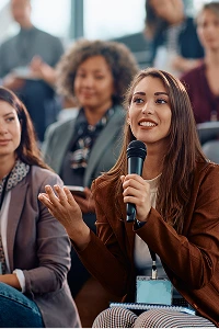 A woman delivers a speech into a microphone at a conference, engaging the audience with her presentation.