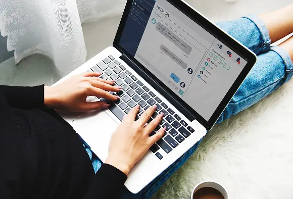 A woman focused on her laptop, typing with both hands on the keyboard.