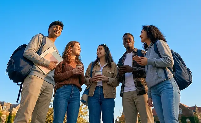 Four young individuals stand together, smiling against a clear blue sky backdrop.