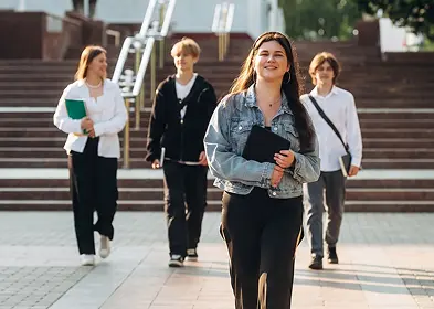 Several students of varying backgrounds stroll down a city street, chatting and carrying backpacks, showcasing camaraderie.