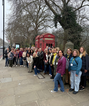 A diverse group of people gathered in front of a red telephone booth, smiling and engaging with one another.