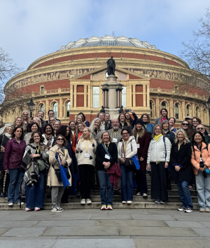 A diverse group of people stands together in front of a modern building, smiling and engaging with one another.