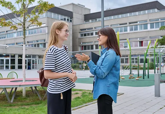 Two women engaged in conversation outside a building, sharing smiles and gesturing as they communicate.