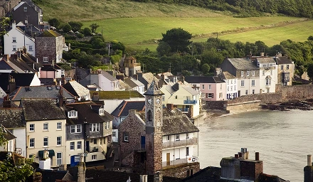 A picturesque hillside town featuring charming houses, surrounded by lush greenery and a bright sky.