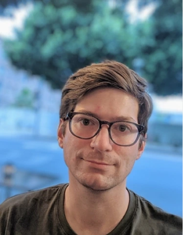 Erik Steigler wearing glasses and a green shirt, smiling while standing against a neutral background.