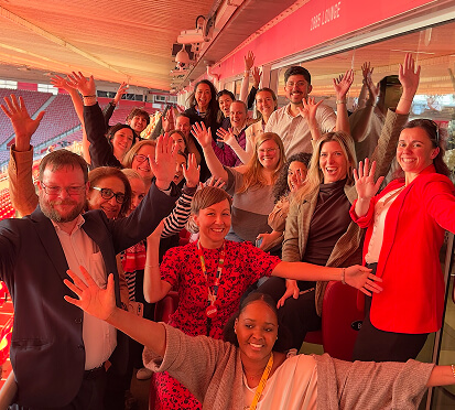 A group of diverse individuals smiling and posing for a photo with their hands raised in celebration.