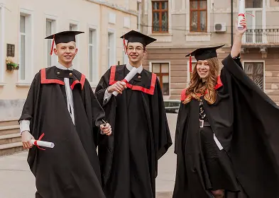 Several graduates in academic regalia stroll down the street, smiling and enjoying their graduation day.
