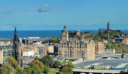 Edinburgh cityscape featuring historic buildings along a river under a clear blue sky.