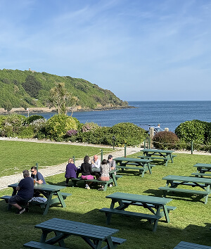 People enjoying a meal at picnic tables with a scenic view of the ocean in the background.