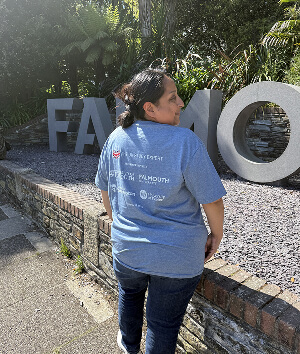 A woman in a blue t-shirt stands in front of a sign for Famo, smiling and posing for the photo.
