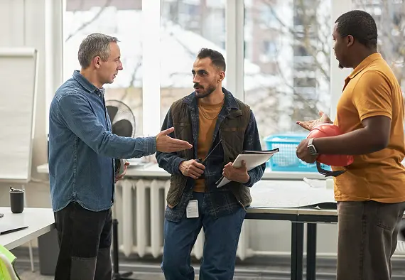 Three men engaged in conversation in a modern office environment, discussing work-related topics.