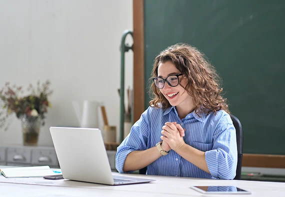 A woman wearing glasses sits at a desk, focused on her laptop while working.