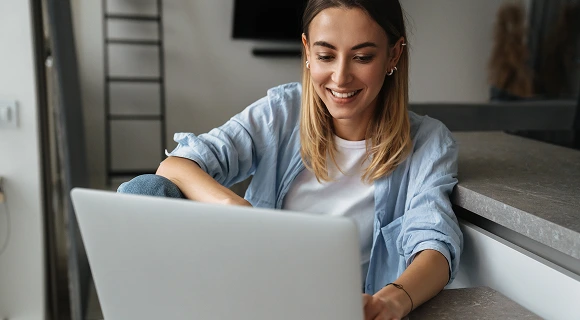A woman smiles while working on a laptop, showcasing a positive and engaged expression.
