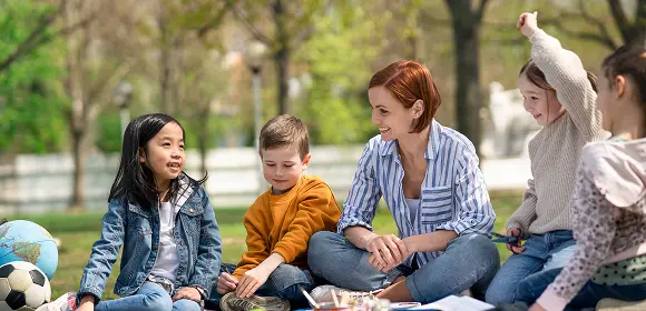 Children gathered on grass, focused on reading, accompanied by the text "teaching children to read."