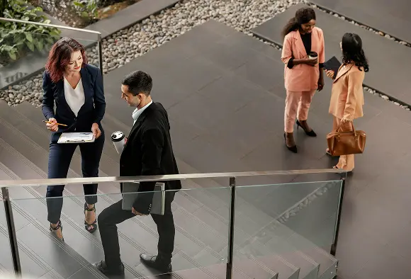 A diverse group of business professionals standing confidently on a staircase, engaged in conversation.