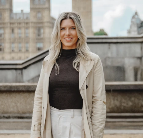 Jackie wearing a stylish trench coat and white pants stands confidently, showcasing a modern fashion look.