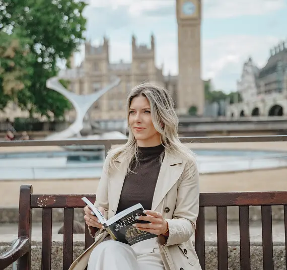 A woman reading a book on a bench with Big Ben in the background, showcasing a peaceful moment in London.