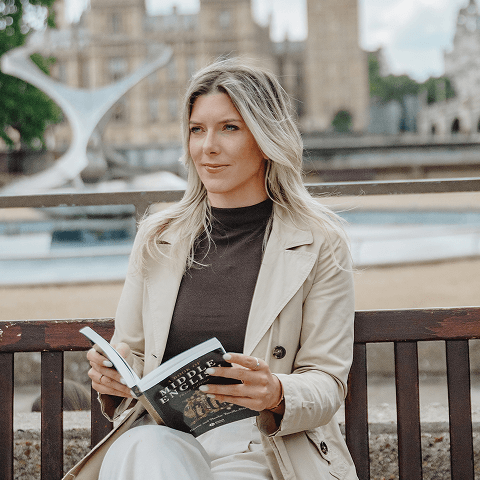 Jackie sits on a bench, engrossed in reading a book in a serene outdoor setting.