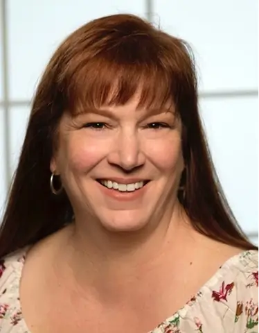 Kim Hayes with vibrant red hair smiles warmly at the camera, exuding a cheerful and friendly demeanor.