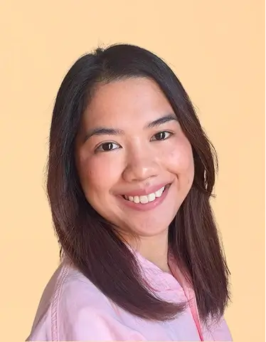 MJ Roldan with long hair wearing a pink shirt, smiling and looking towards the camera.
