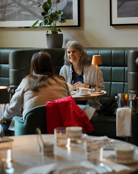 Two women engaged in conversation while seated at a restaurant table, enjoying their meal together.