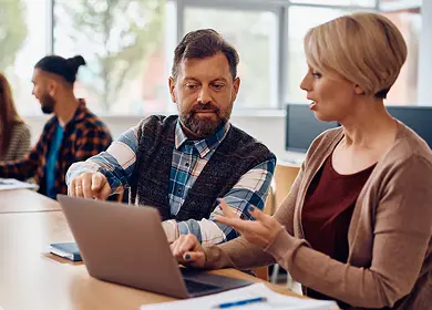 A man and woman collaborate over a laptop, both engaged in the task at hand.
