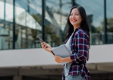 A smiling woman in a plaid shirt holds a tablet, showcasing a friendly and engaged demeanor.