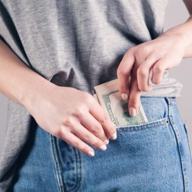 Person tucking U.S. dollar bills into the front pocket of blue jeans